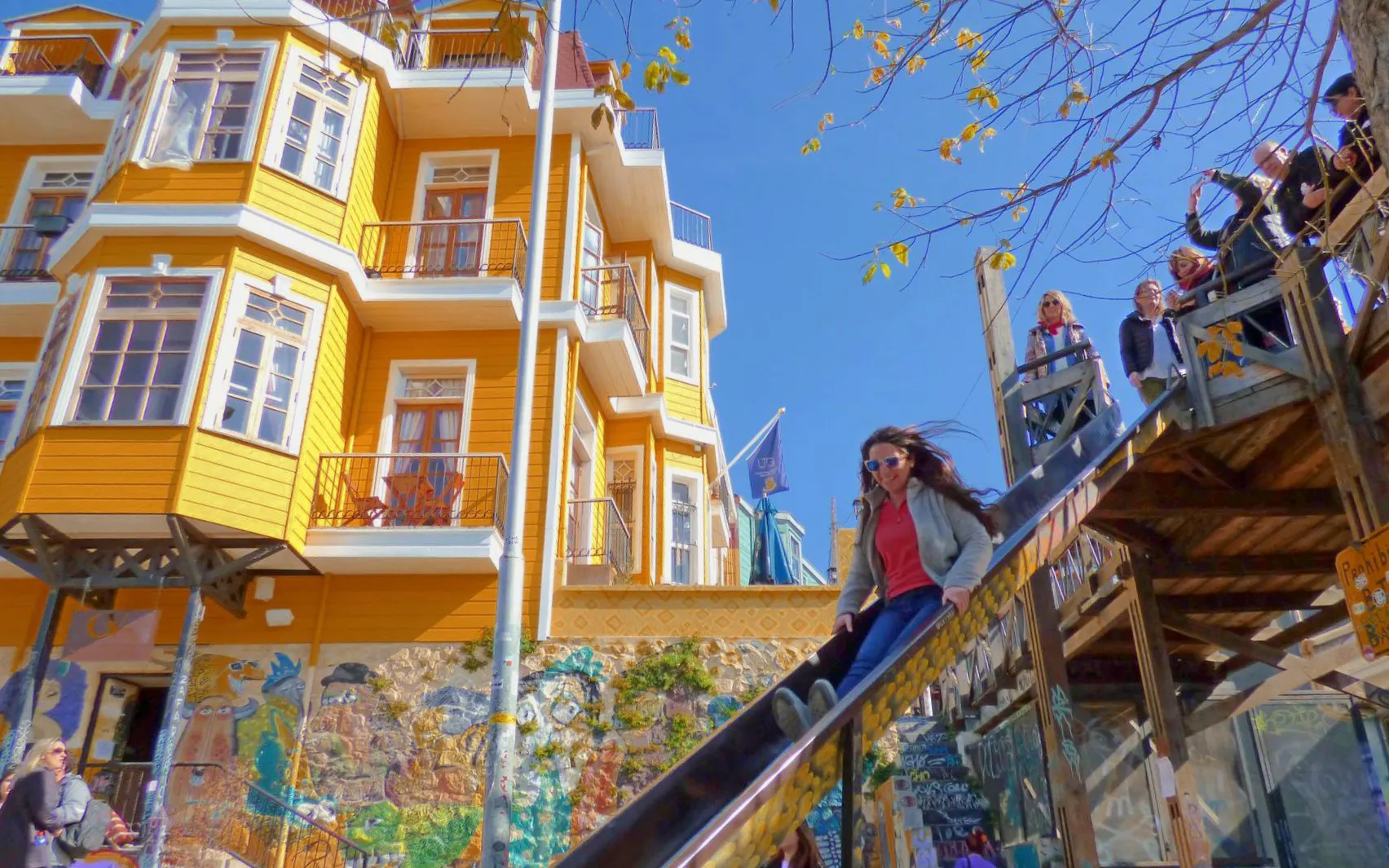 Tourist sliding down a slide near colorful hillside homes and street art in Valparaíso, Chile.