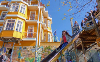 Tourist sliding down a slide near colorful hillside homes and street art in Valparaíso, Chile.