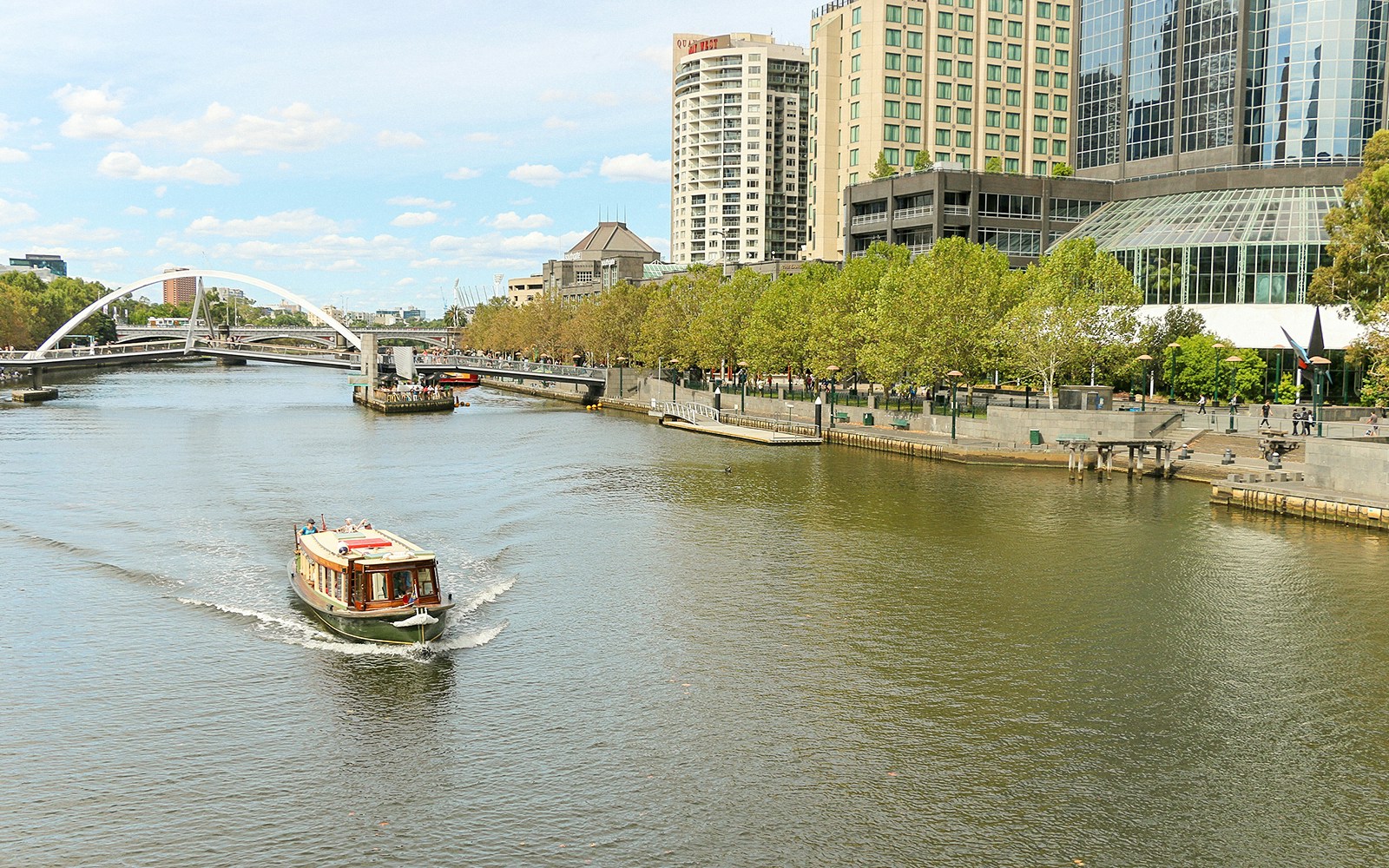 Cruise boat on Yarra River passing Southbank, Melbourne with cityscape and bridge.