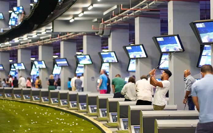 Golfers playing at Topgolf Dubai with multiple screens and targets in view.