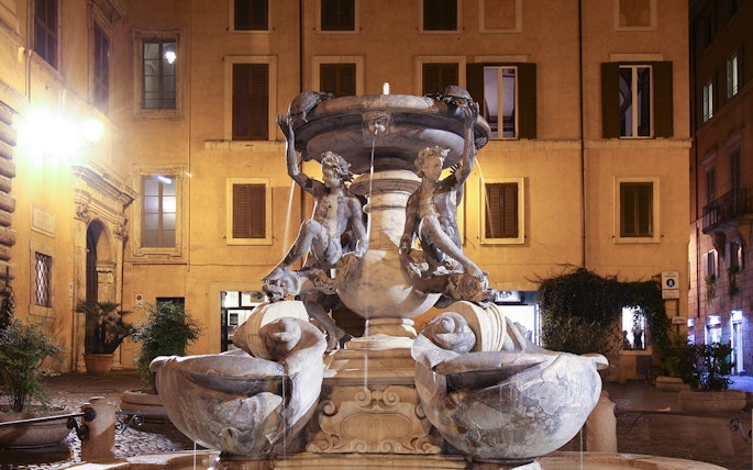 Turtle Fountain in Rome illuminated at night with sculptures and water features.