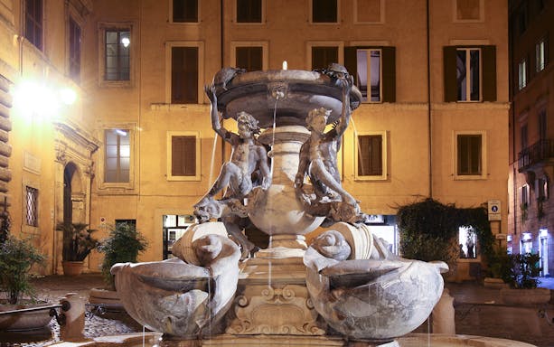 Turtle Fountain in Rome illuminated at night with sculptures and water features.