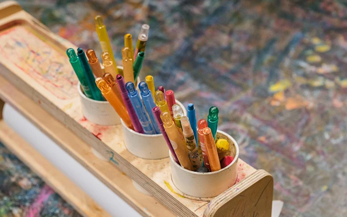 Colorful markers in cups on a wooden holder at Teddy Bear Museum art station.