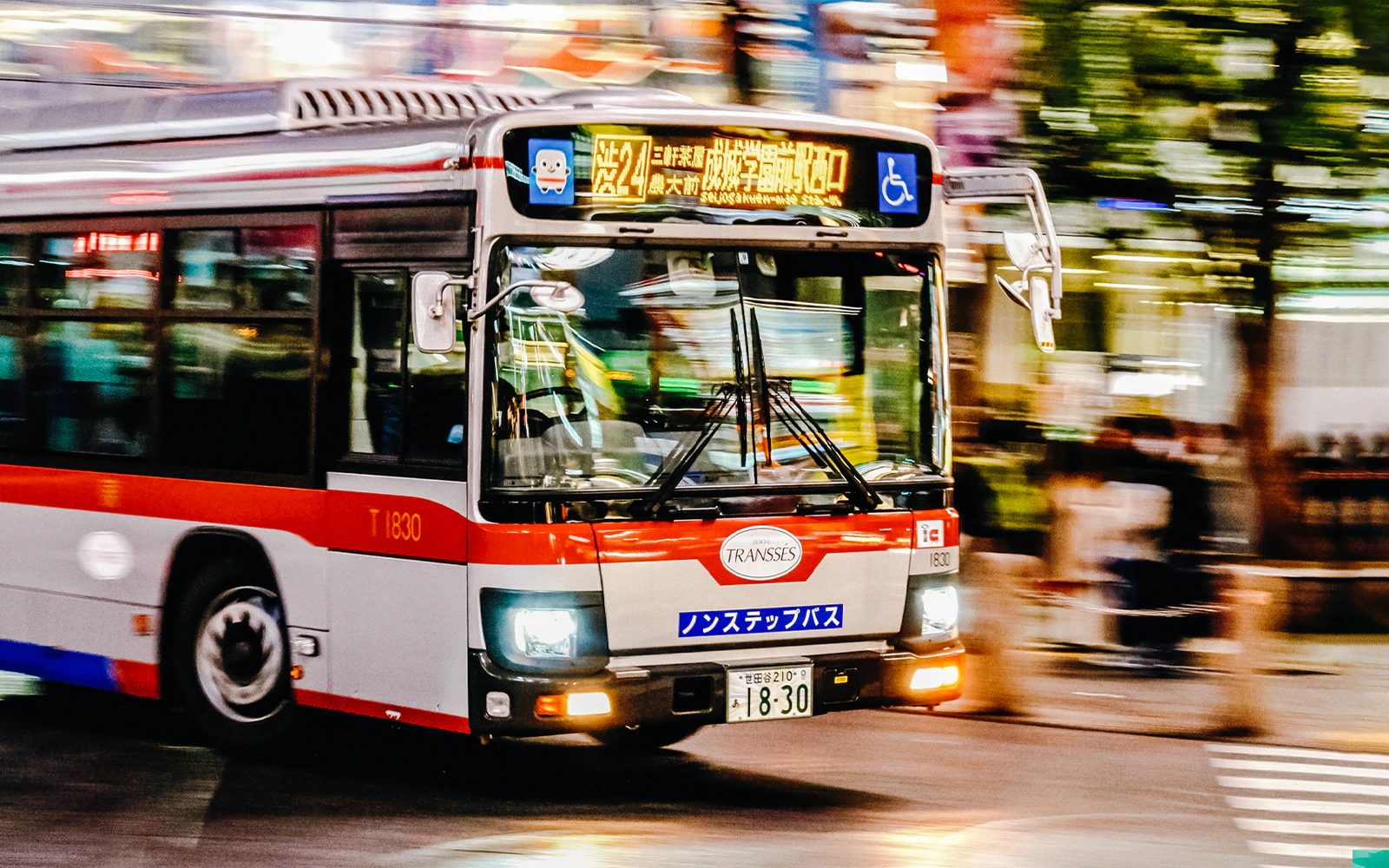 Red and white bus driving through Shibuya, Tokyo, Japan at night.