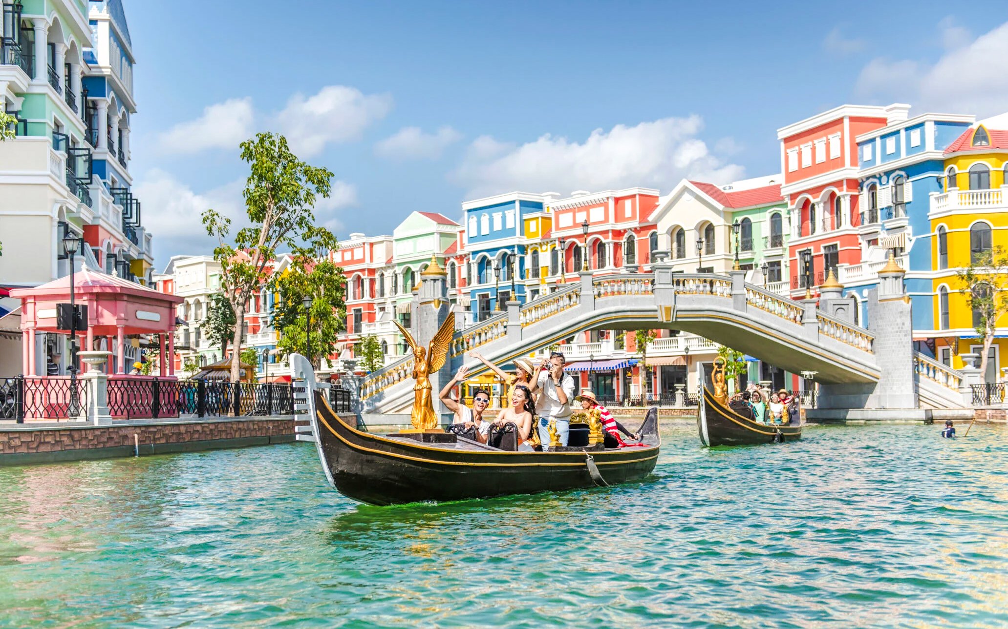 Gondola ride in Venice with colorful buildings and a stone bridge in the background.
