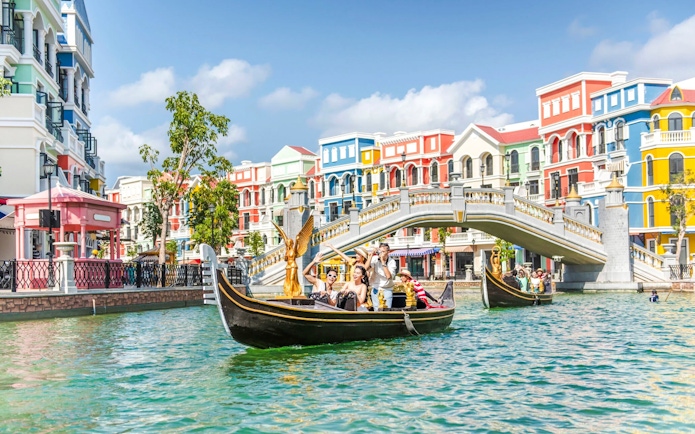 Gondola ride in Venice with colorful buildings and a stone bridge in the background.