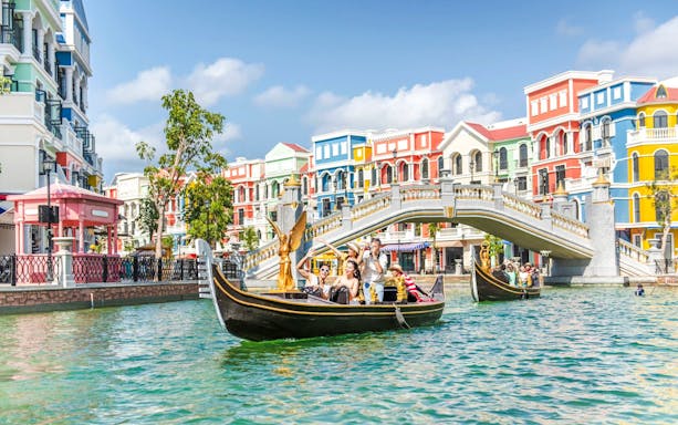 Gondola ride in Venice with colorful buildings and a stone bridge in the background.