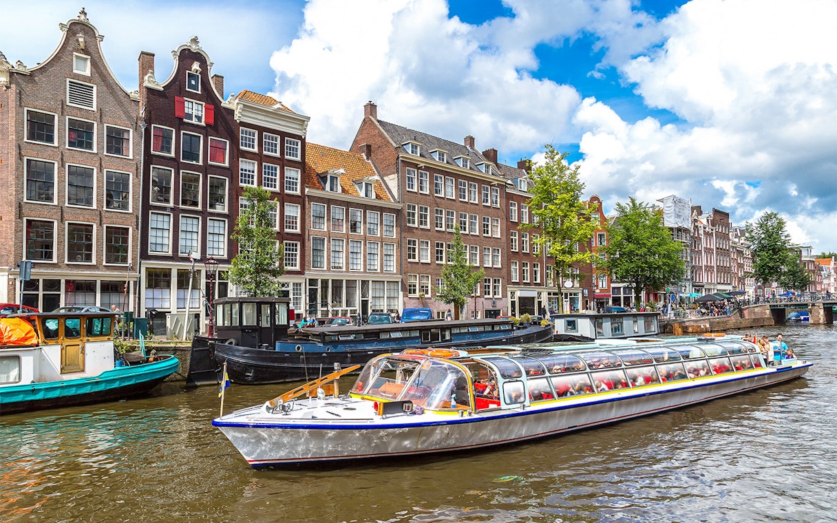 Canal cruise boat on Amsterdam canal with historic buildings in the background.