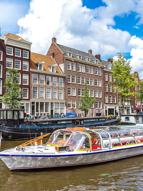 Canal cruise boat on Amsterdam canal with historic buildings in the background.