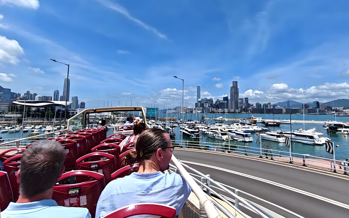 Guests on an open-top bus tour in Hong Kong with a view of the skyline and harbor.