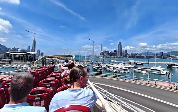 Guests on an open-top bus tour in Hong Kong with a view of the skyline and harbor.