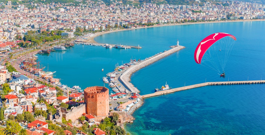 Paraglider tandem flying over marina and Red tower in Alanya peninsula, Antalya district