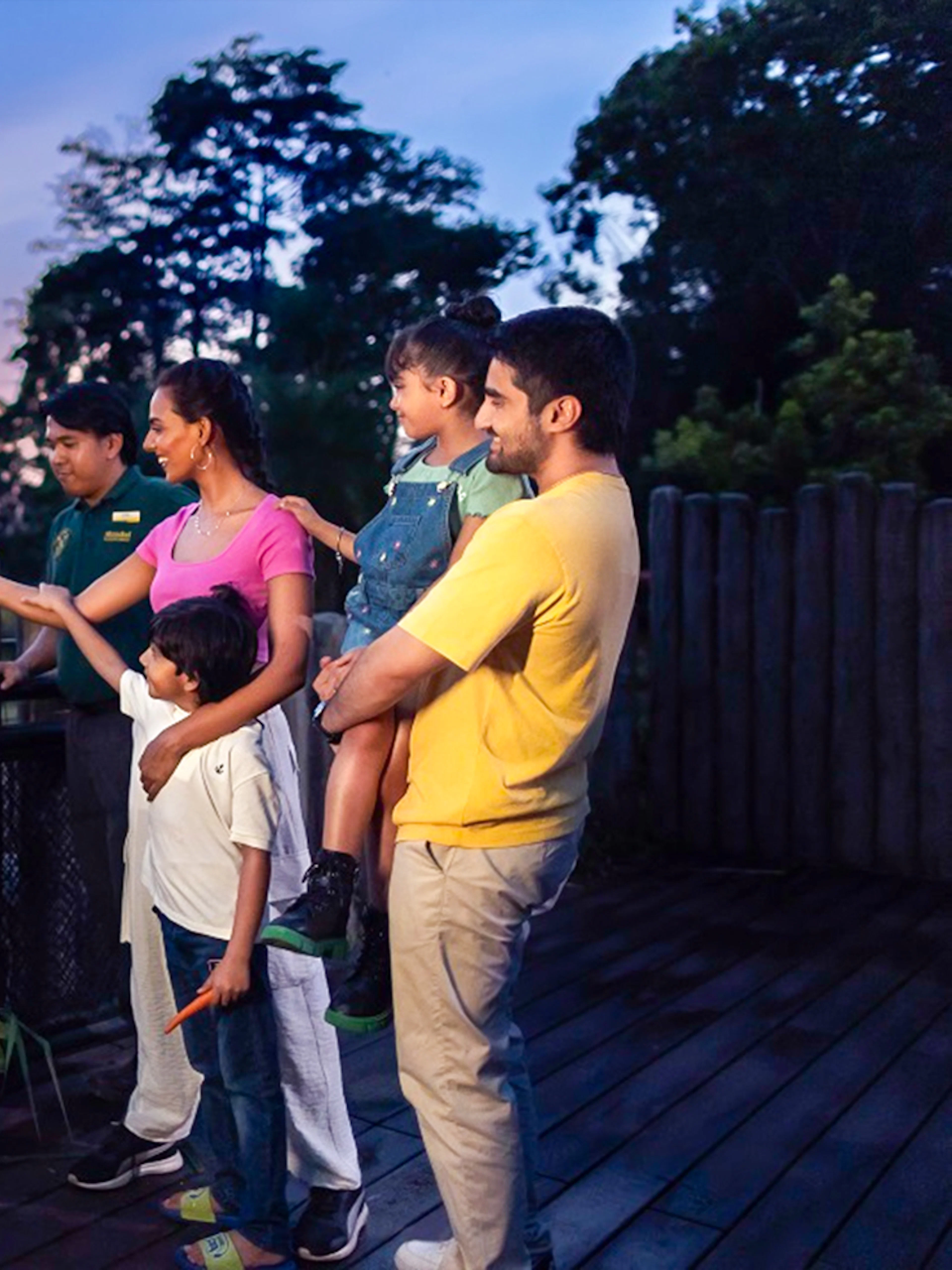 Family feeding an Indian rhino at a wildlife park during sunset.