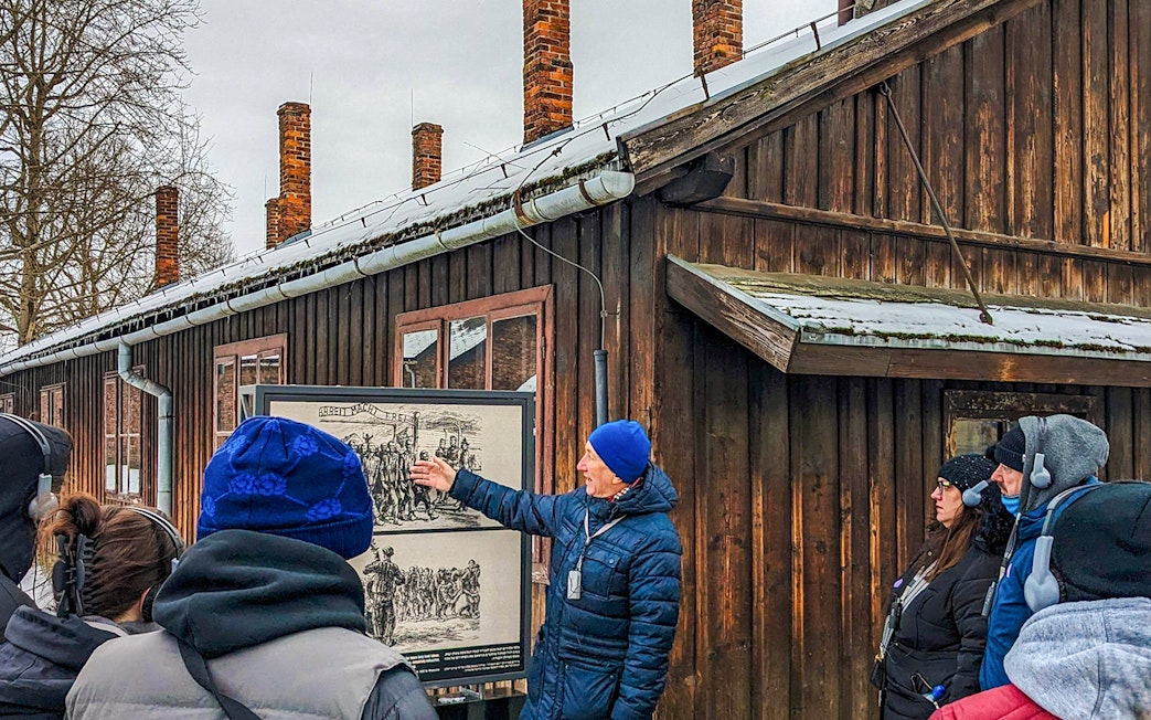 Guide explaining historical photo at Auschwitz Birkenau to tour group.