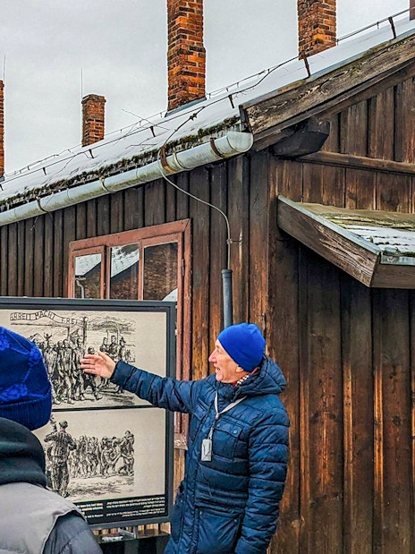 Guide explaining historical photo at Auschwitz Birkenau to tour group.