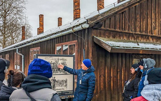 Guide explaining historical photo at Auschwitz Birkenau to tour group.