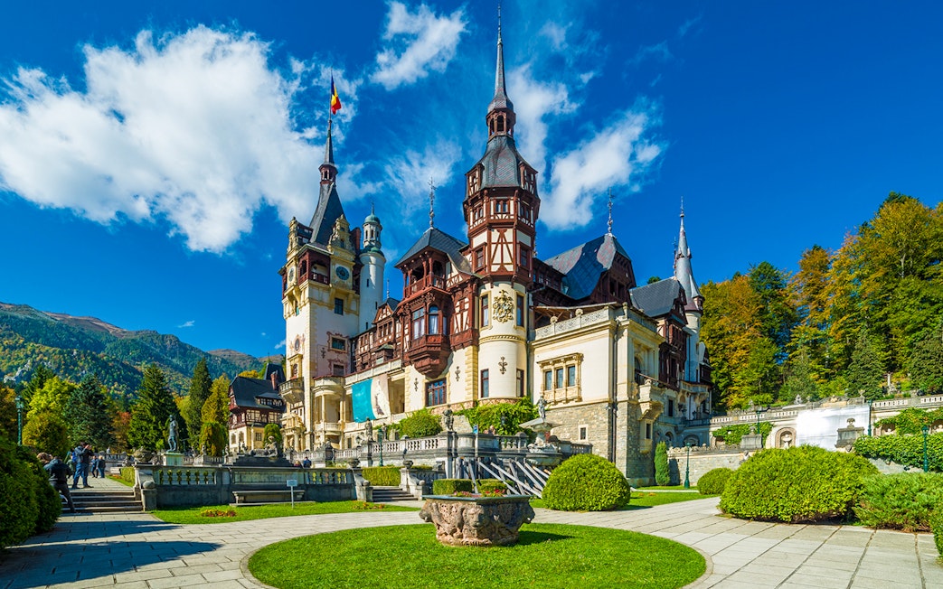 Peles Castle exterior with ornate towers and lush gardens in Sinaia, Romania.