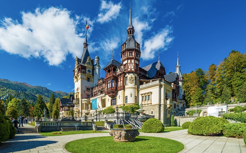 Peles Castle exterior with ornate towers and lush gardens in Sinaia, Romania.