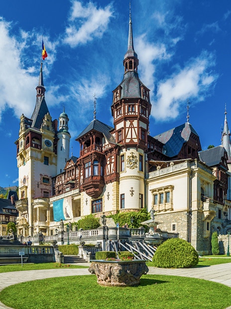 Peles Castle exterior with ornate towers and lush gardens in Sinaia, Romania.