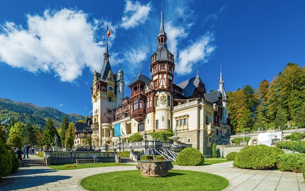 Peles Castle exterior with ornate towers and lush gardens in Sinaia, Romania.