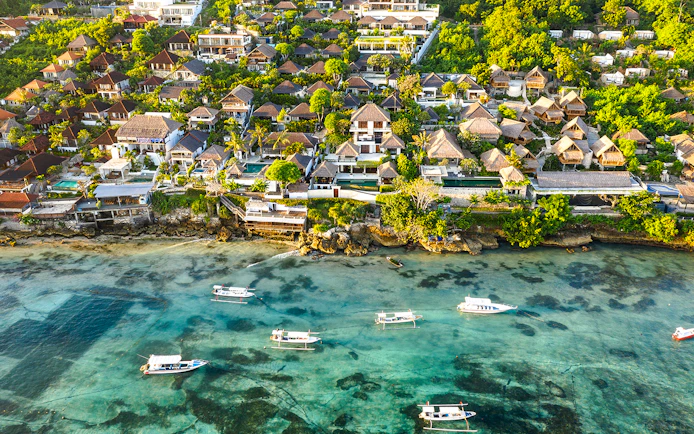 Aerial view of Nusa Lembongan coastline with boats and lush greenery.