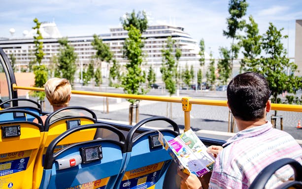 Tourists on a yellow sightseeing bus with a cruise ship in the background.