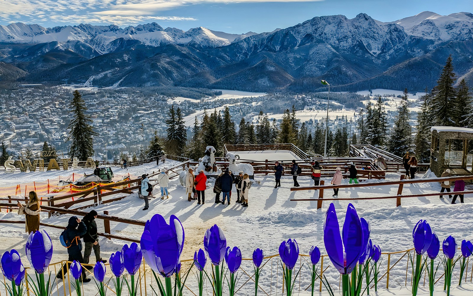 Panoramic view of Tatra Mountains from Zakopane with visitors and snow-covered landscape.
