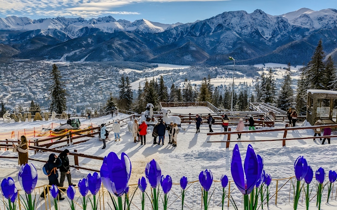 Panoramic view of Tatra Mountains from Zakopane with visitors and snow-covered landscape.