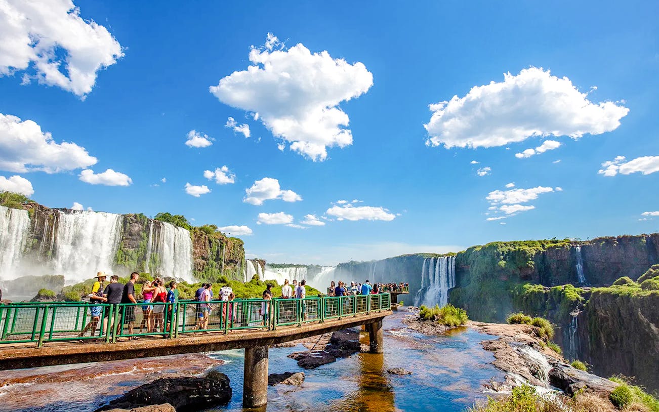 Visitors on a walkway at Iguazu Falls, Brazil, with cascading waterfalls in the background.