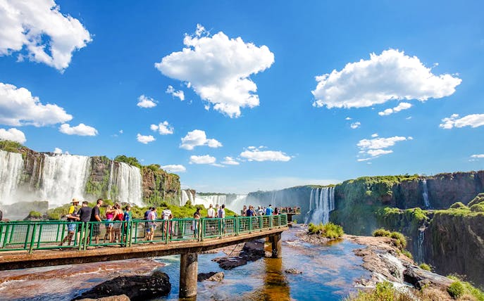 Visitors on a walkway at Iguazu Falls, Brazil, with cascading waterfalls in the background.