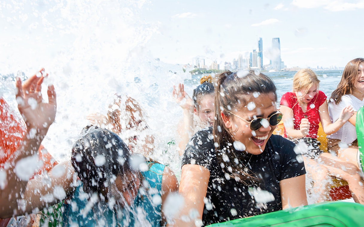 Guests enjoying splashes on NYC Speedboat Ride with city skyline in background.
