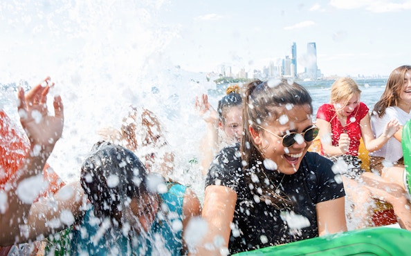 Guests enjoying splashes on NYC Speedboat Ride with city skyline in background.