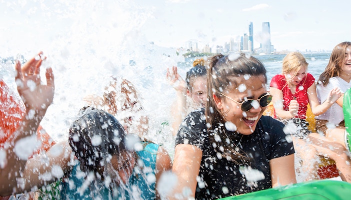 Guests enjoying splashes on NYC Speedboat Ride with city skyline in background.