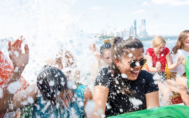 Guests enjoying splashes on NYC Speedboat Ride with city skyline in background.
