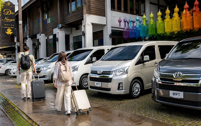 Travelers with luggage approaching private vans for transfer from Chiang Mai to Chiang Rai.