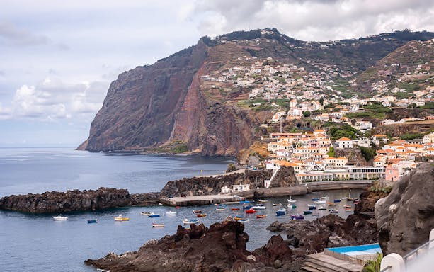 Coastal view of Madeira with colorful boats and hillside village on the 3-in-1 Hop-On Hop-Off Tour.
