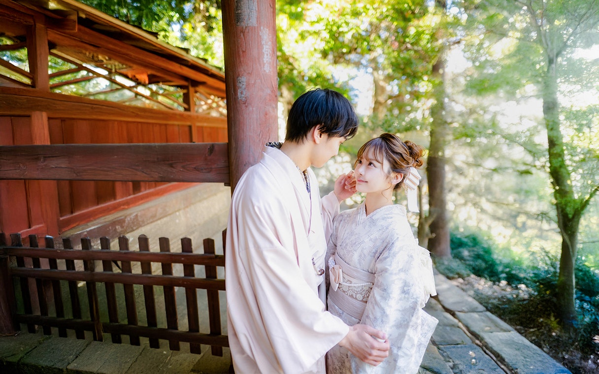 Couple in Yukata posing in a lush green garden with traditional wooden architecture.