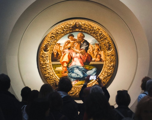 Visitors engrossed by Michelangelo’s Tondo Doni, the masterful circular painting that captivates with its vivid colors and divine composition at Uffizi Gallery
