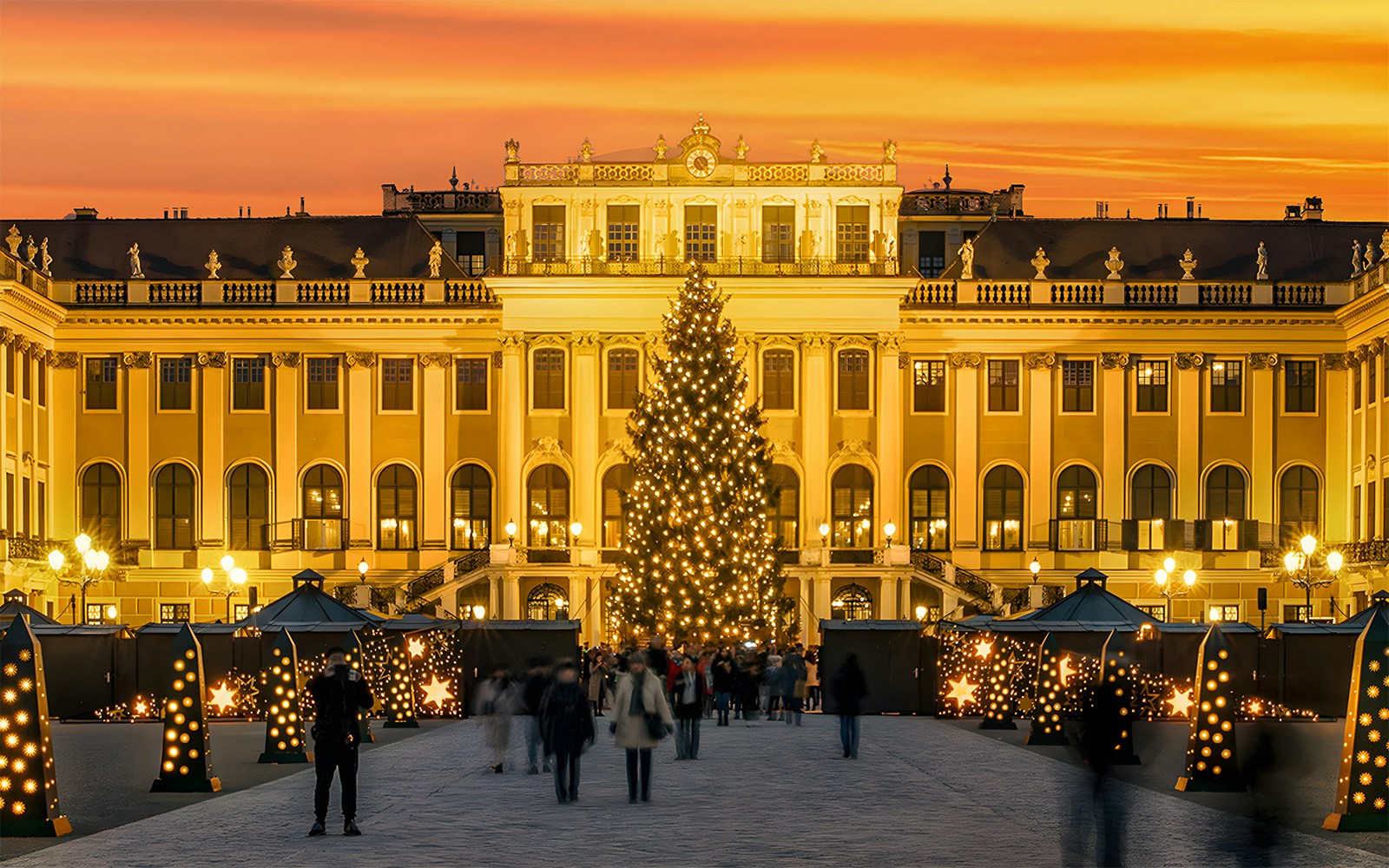 Schonbrunn Palace Christmas Market with lit tree and visitors at sunset.