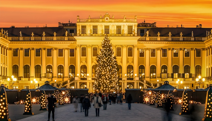 Schonbrunn Palace Christmas Market with lit tree and visitors at sunset.