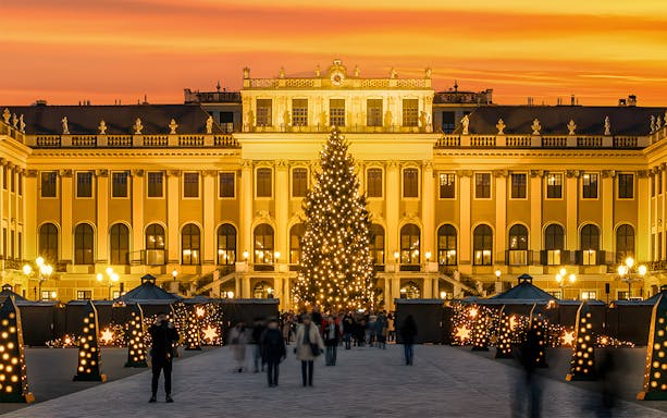 Schonbrunn Palace Christmas Market with lit tree and visitors at sunset.