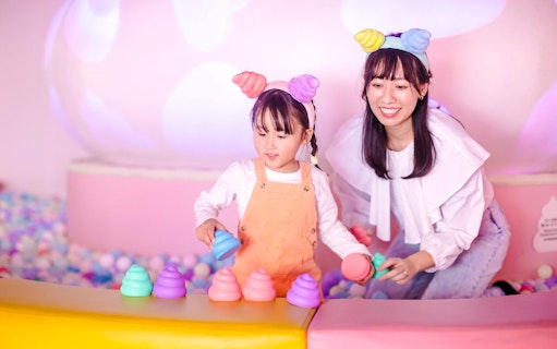 Mother and daughter with themed headbands play with colorful toys in a ball pit at Unko Museum.