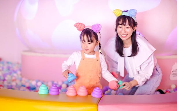 Mother and daughter with themed headbands play with colorful toys in a ball pit at Unko Museum.
