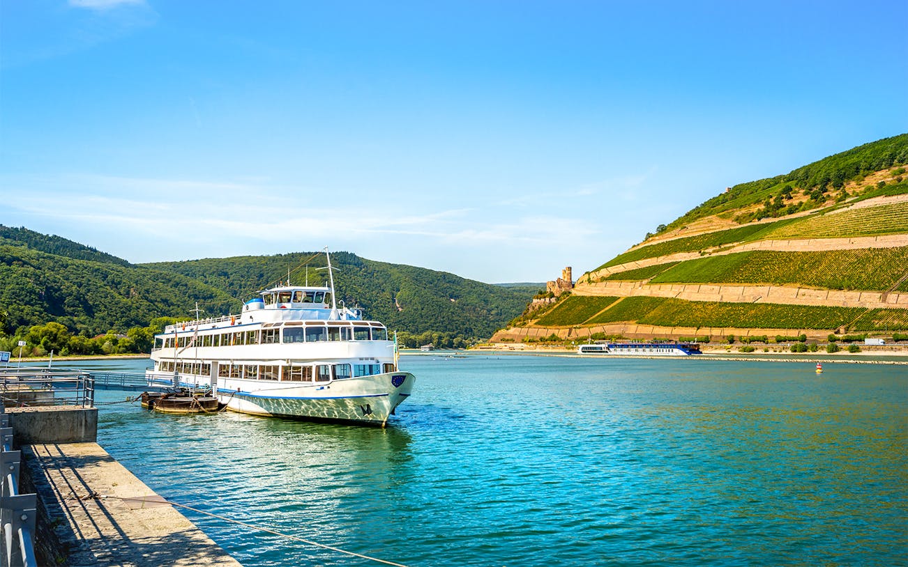River cruise ship docked in Bingen on the Rhine, Germany with vineyards and hills in the background.