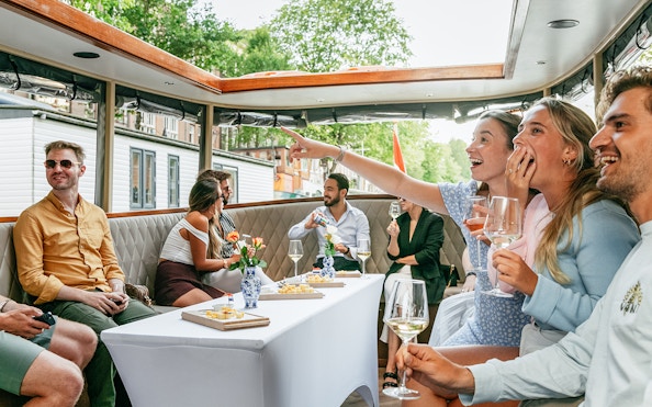 Open boat cruise in Amsterdam with people enjoying drinks and sightseeing.