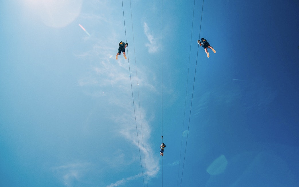 Visitors ziplining at Mega Adventure Park, Singapore against a clear blue sky.