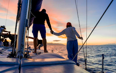 Sailboat cruise at sunset with people enjoying the view, ocean in the background.