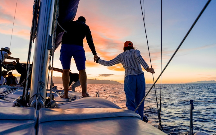 Sailboat cruise at sunset with people enjoying the view, ocean in the background.