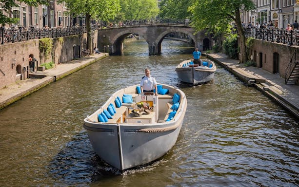 Open boat cruising through Utrecht canal under a stone bridge.