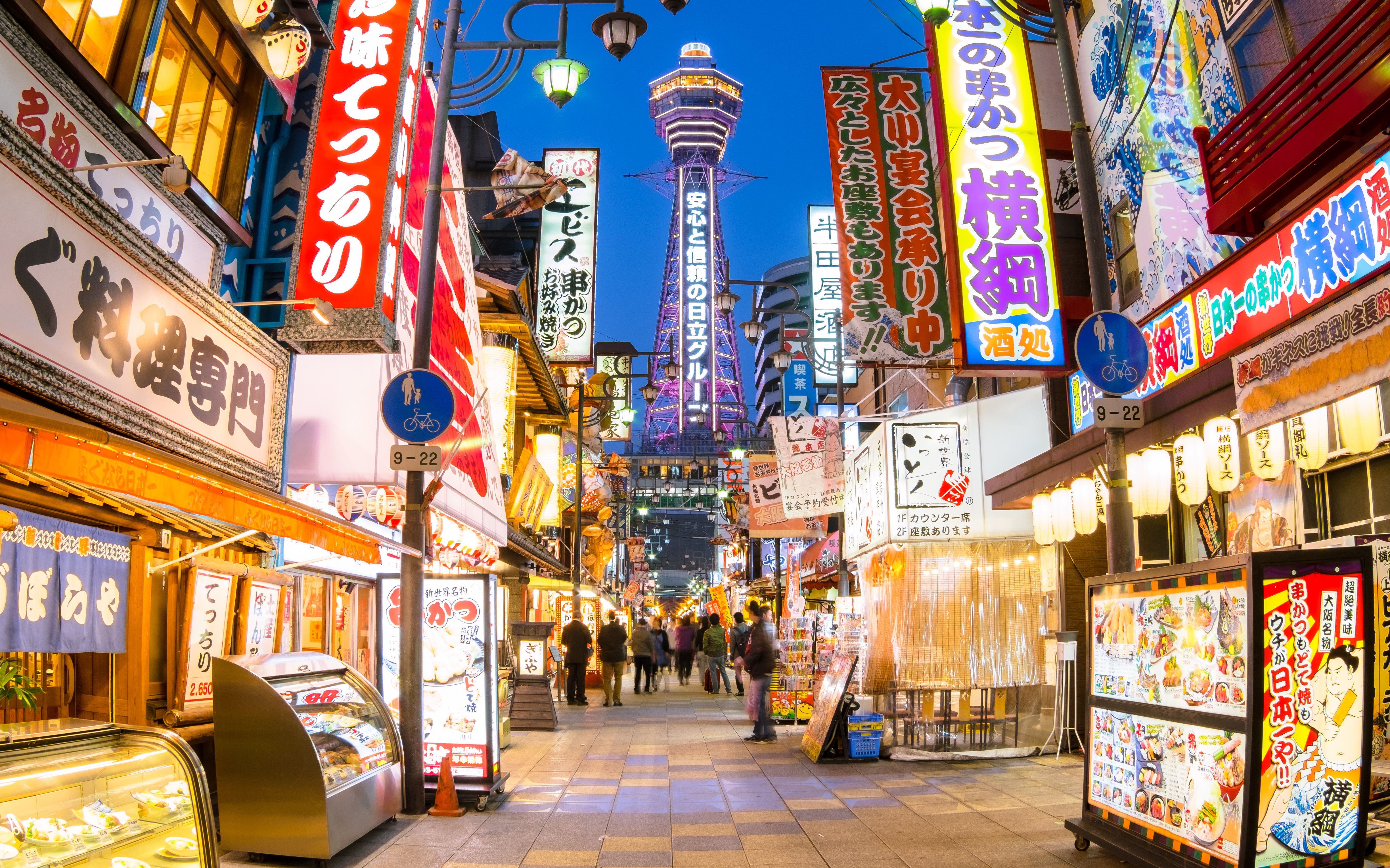Bustling street in Osaka with Tsutenkaku Tower in the background.
